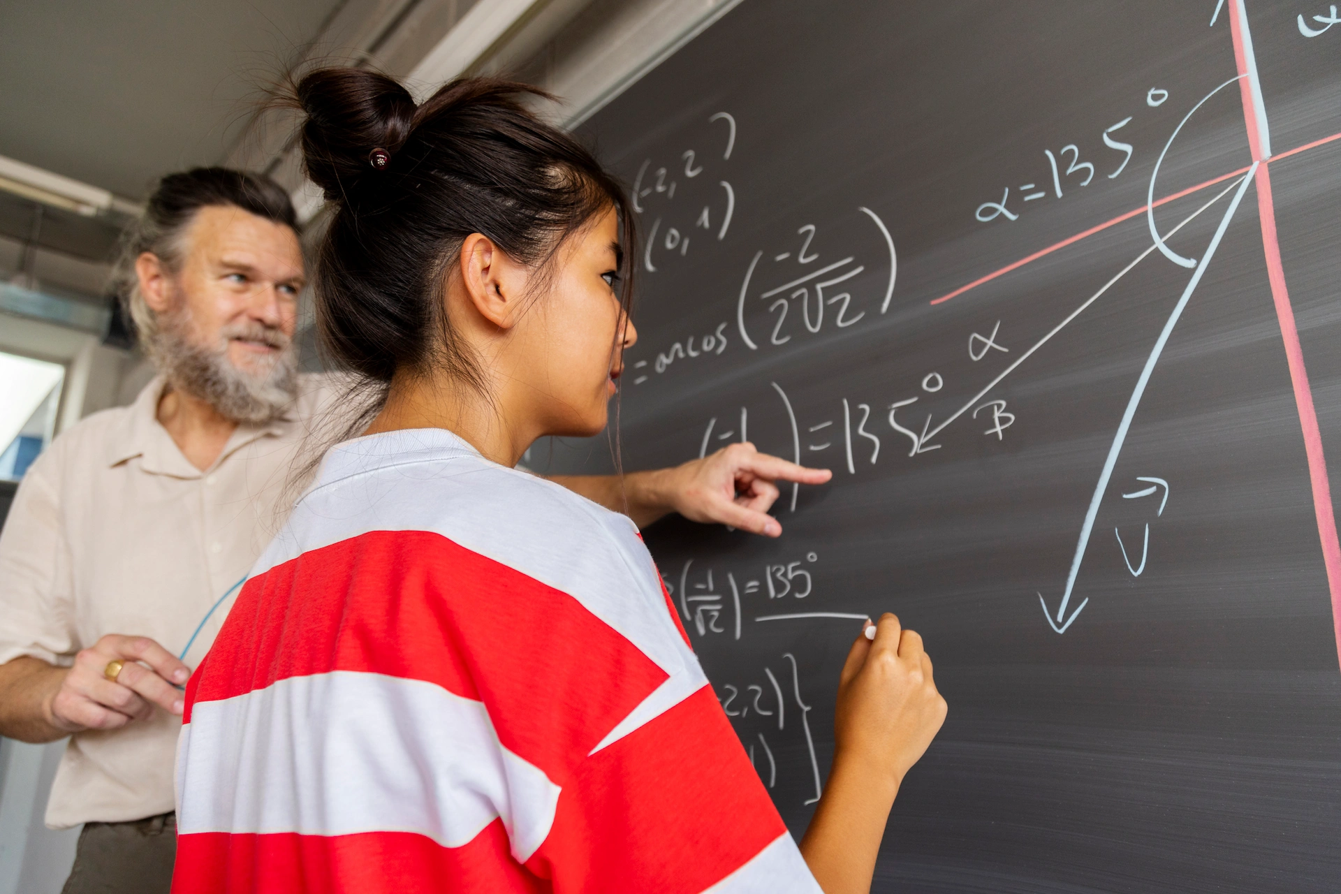 trigonometry student working on an equation at the chalkboard with her tutor helping her out