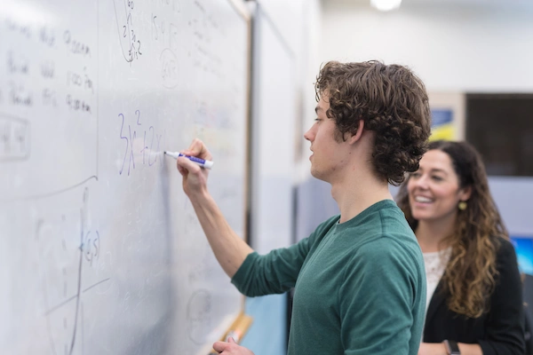 male student writing out a math problem on the white board