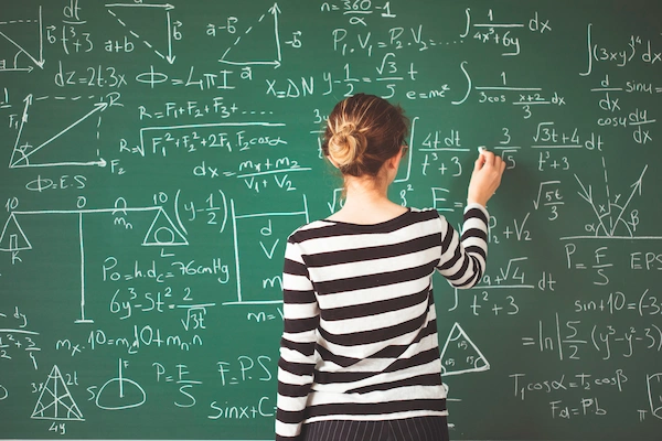 Young student writing with chalk on green chalkboard in classroom mastering high school math problem
