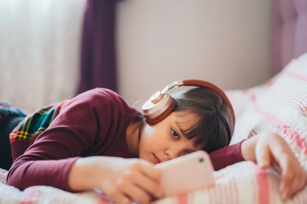 tired looking student lying in bed looking at her smart phone